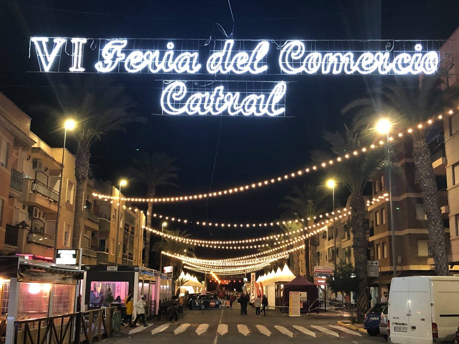 Calle con letrero luminoso de feria del comercio y guirnaldas de bombillas